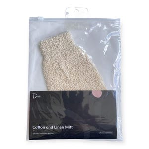 Puede incluir: Un guante de algodón y lino beige está empaquetado en una bolsa de plástico transparente. El guante es texturizado y parece ser para exfoliar. El embalaje incluye una etiqueta negra con la palabra "Diva" y el texto "Cotton and Linen Mitt".