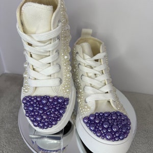 May include: White high-top sneakers with purple and white pearl embellishments.
