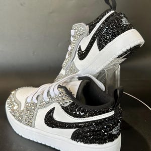 Puede incluir: Zapatillas blancas y negras con pedrer&iacute;a negra en el lateral y pedrer&iacute;a blanca en la puntera. Las zapatillas tienen un logotipo Swoosh negro y un logotipo Jordan negro y blanco en la parte posterior.