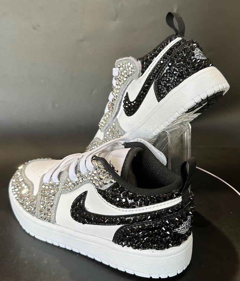 Puede incluir: Zapatillas blancas y negras con pedrer&iacute;a negra en el lateral y pedrer&iacute;a blanca en la puntera. Las zapatillas tienen un logotipo Swoosh negro y un logotipo Jordan negro y blanco en la parte posterior.