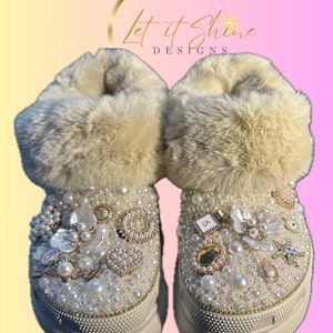 Könnte beinhalten: Weiße Stiefel mit Kunstfellfutter, weißer Plateau-Sohle und Perlenbesatz. Die Stiefel sind mit Perlenblumen, Charms und Strasssteinen verziert. Der Text "Let it Shine Designs" ist über den Stiefeln sichtbar.