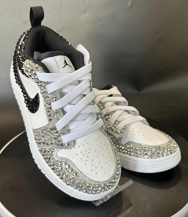 Puede incluir: Zapatillas blancas de cuero con detalles negros y un dise&ntilde;o de cristal. Las zapatillas tienen un cierre de cordones blanco y un logotipo swoosh negro.