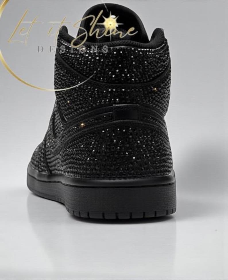 May include: Black high-top sneaker covered in sparkling embellishments. The shoe features a solid black sole and a textured upper, with the words "Let it Shine Designs" in gold script.