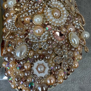 Pu&ograve; includere: Primo piano di un ornamento bianco incrostato di perle con accenti dorati. L'ornamento &egrave; ricoperto di perle, strass e altri elementi decorativi.