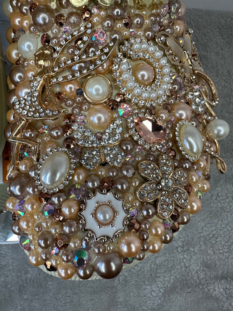 Pu&ograve; includere: Primo piano di un ornamento bianco incrostato di perle con accenti dorati. L'ornamento &egrave; ricoperto di perle, strass e altri elementi decorativi.