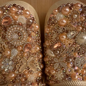 Pu&ograve; includere: Un paio di scarpe bianche decorate con perle, strass e dettagli dorati. Le scarpe sono ricoperte da una variet&agrave; di decorazioni, creando un look lussuoso e glamour.