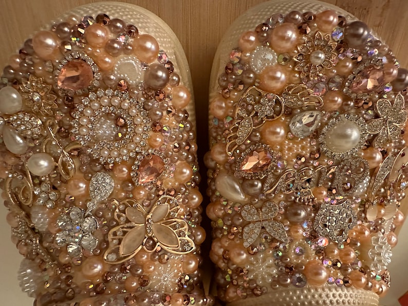 Pu&ograve; includere: Un paio di scarpe bianche decorate con perle, strass e dettagli dorati. Le scarpe sono ricoperte da una variet&agrave; di decorazioni, creando un look lussuoso e glamour.