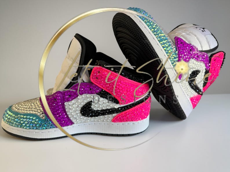 May include: Two bedazzled sneakers. One sneaker is primarily pink and purple with a black Nike swoosh. The other sneaker is primarily blue and white. Both sneakers have white soles and black laces. The sneakers are decorated with iridescent rhinestones.