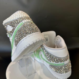May include: White high-top sneakers with a green and silver rhinestone design.