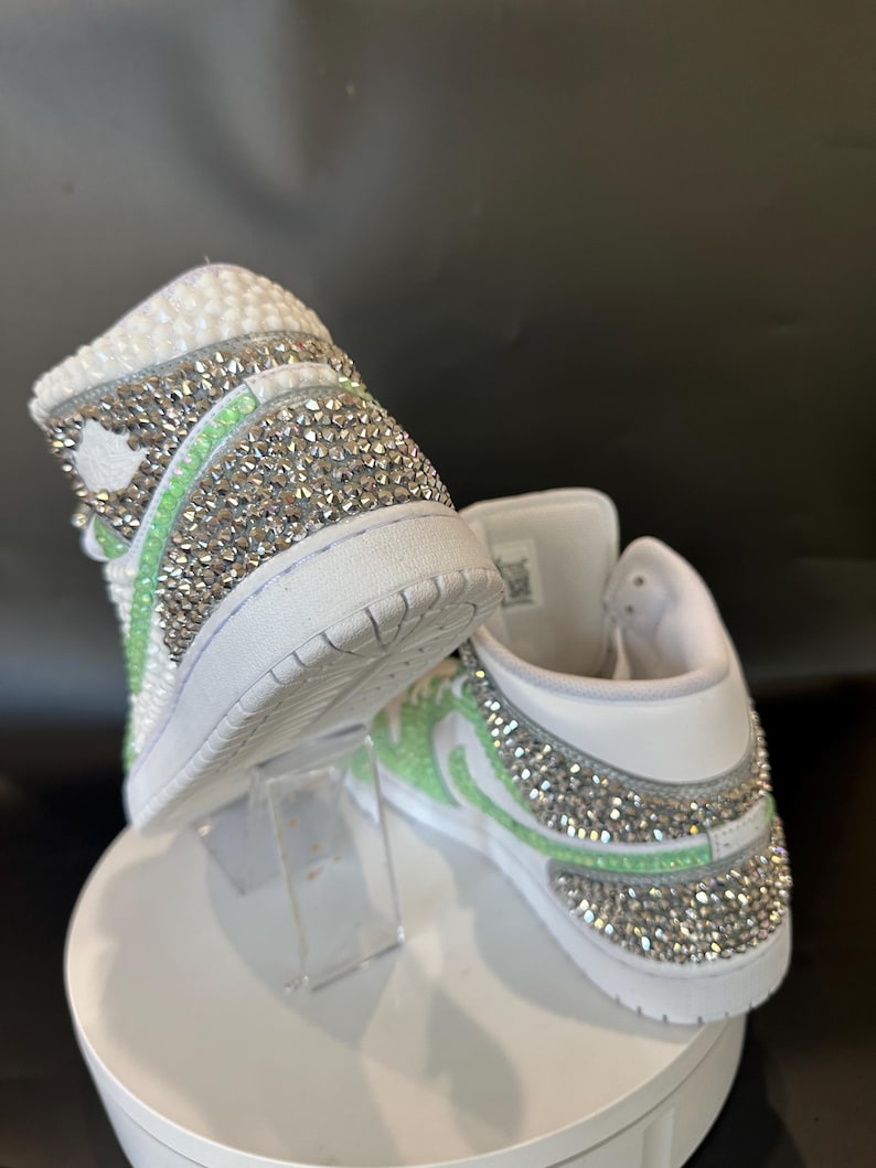 May include: White high-top sneakers with a green and silver rhinestone design.