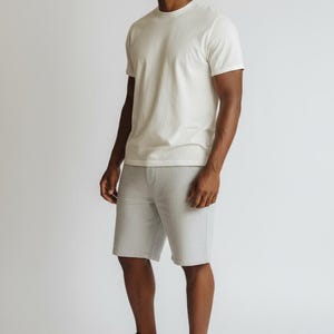 May include: A person wearing a white crew neck t-shirt, gray shorts, and colorful sneakers. The sneakers have pink, purple, and blue accents. The outfit is casual and comfortable, suitable for everyday wear.