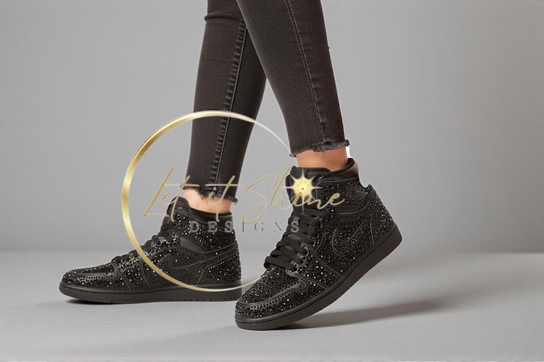 May include: Black high-top sneakers with sparkling embellishments. The shoes feature a lace-up design and a black sole. The sneakers are worn with black denim jeans. The overall aesthetic is stylish and eye-catching.
