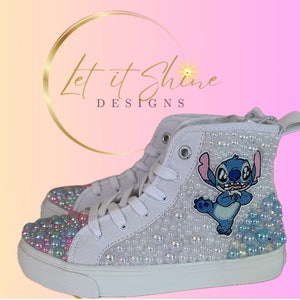 May include: White high-top sneakers with a blue Stitch character embroidered on the side. The shoes are covered in iridescent pearls.