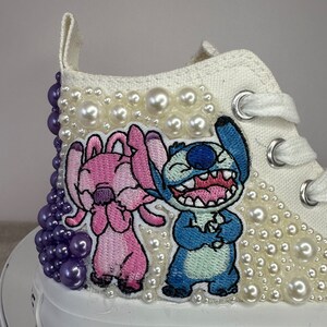May include: White high-top sneakers with a pearl embellishment and embroidered images of Stitch and Angel from the Disney movie Lilo & Stitch.