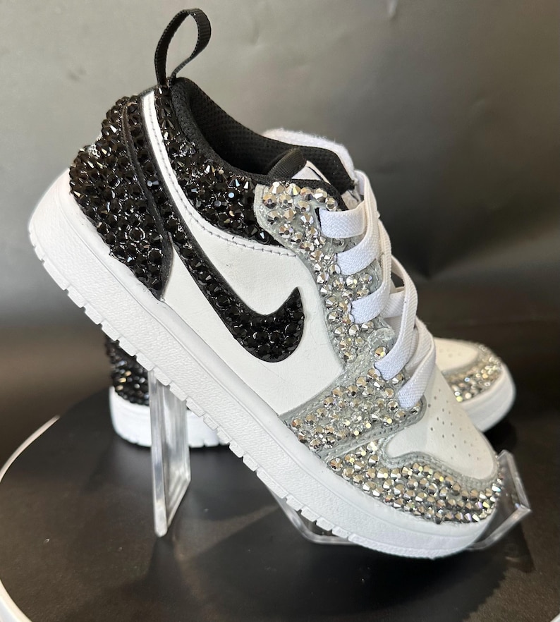 Puede incluir: Zapatillas bajas de cuero blanco con pedrer&iacute;a negra y transparente que cubre toda la zapatilla.