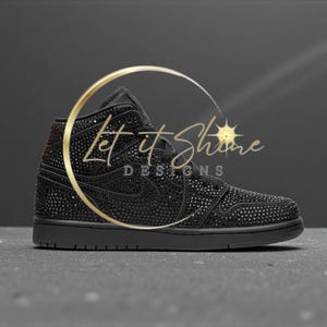 May include: Black high-top sneaker embellished with sparkling accents. The shoe features a classic design with a prominent Nike swoosh and the text "Let It Shine Designs" in gold.