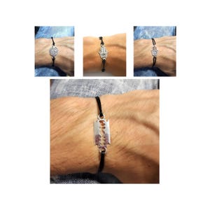May include: A collection of four bracelets. Three bracelets feature silver charms: a coin, a Hamsa hand, and another Hamsa hand. The fourth bracelet has a silver razor blade charm. All bracelets have black cords.