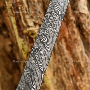 May include: Close-up of a black and silver patterned blade with a wavy, flowing design. The blade is made of Damascus steel.