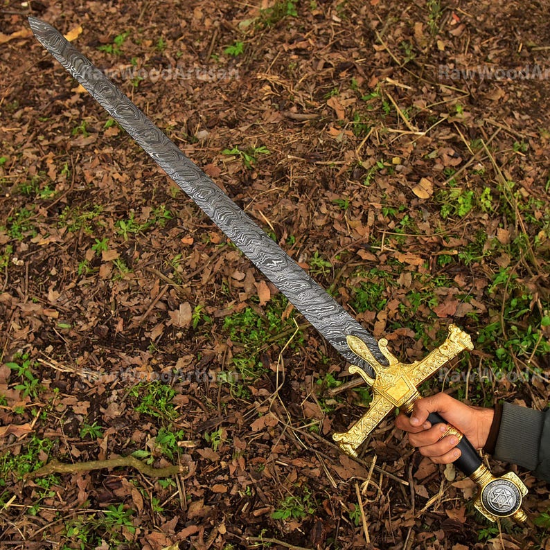 May include: A sword with a gold-coloured hilt and a damascus steel blade. The blade has a wavy pattern and the hilt is decorated with intricate details.