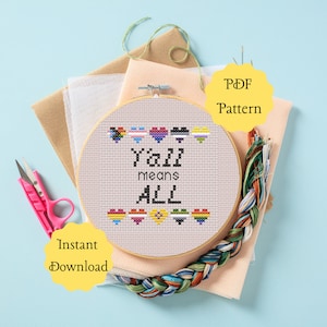 May include: A cross-stitch pattern featuring the phrase "Y'all means ALL" with a row of rainbow hearts and pride flags above the text. The pattern is displayed in a wooden embroidery hoop on a beige fabric background. The words "PDF Pattern" and "Instant Download" are written in yellow circles on the image.