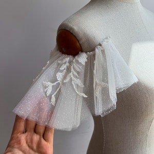 May include: White tulle bridal shoulder sleeves with delicate floral embroidery and a subtle sparkle.