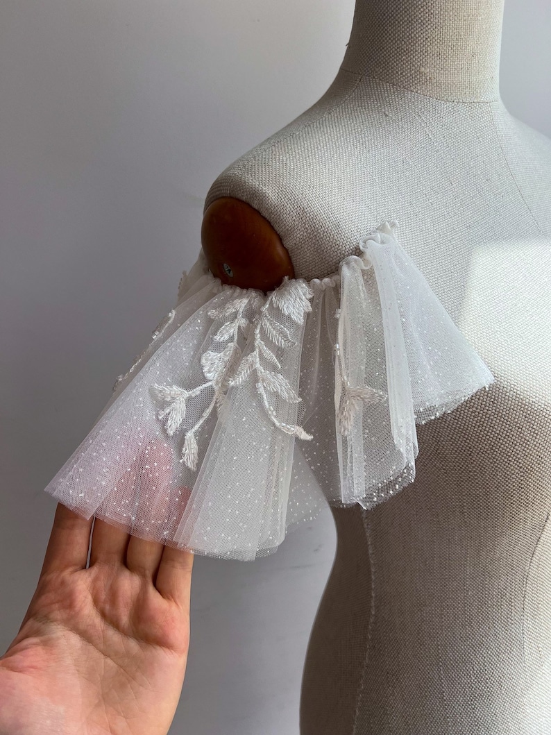 May include: White tulle bridal shoulder sleeves with delicate floral embroidery and a subtle sparkle.
