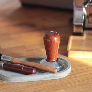 Könnte beinhalten: Ein graues Betontablett mit einem Holztamper, einem Pinsel mit der Aufschrift "ECM" und einem kleinen Holzetui.