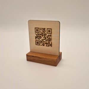 Könnte beinhalten: Ein Holzschild mit einem darauf gedruckten QR-Code. Das Schild steht auf einem kleinen Holzständer.