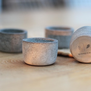 Pode incluir: Quatro pequenos porta-velas de concreto cinza, um com o texto "B | BERNECHE" gravado na lateral.