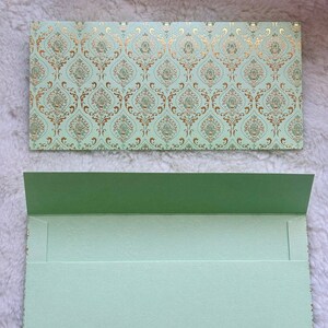 May include: A light green envelope with a gold and green patterned design. The envelope is folded in half and has a flap on the top.
