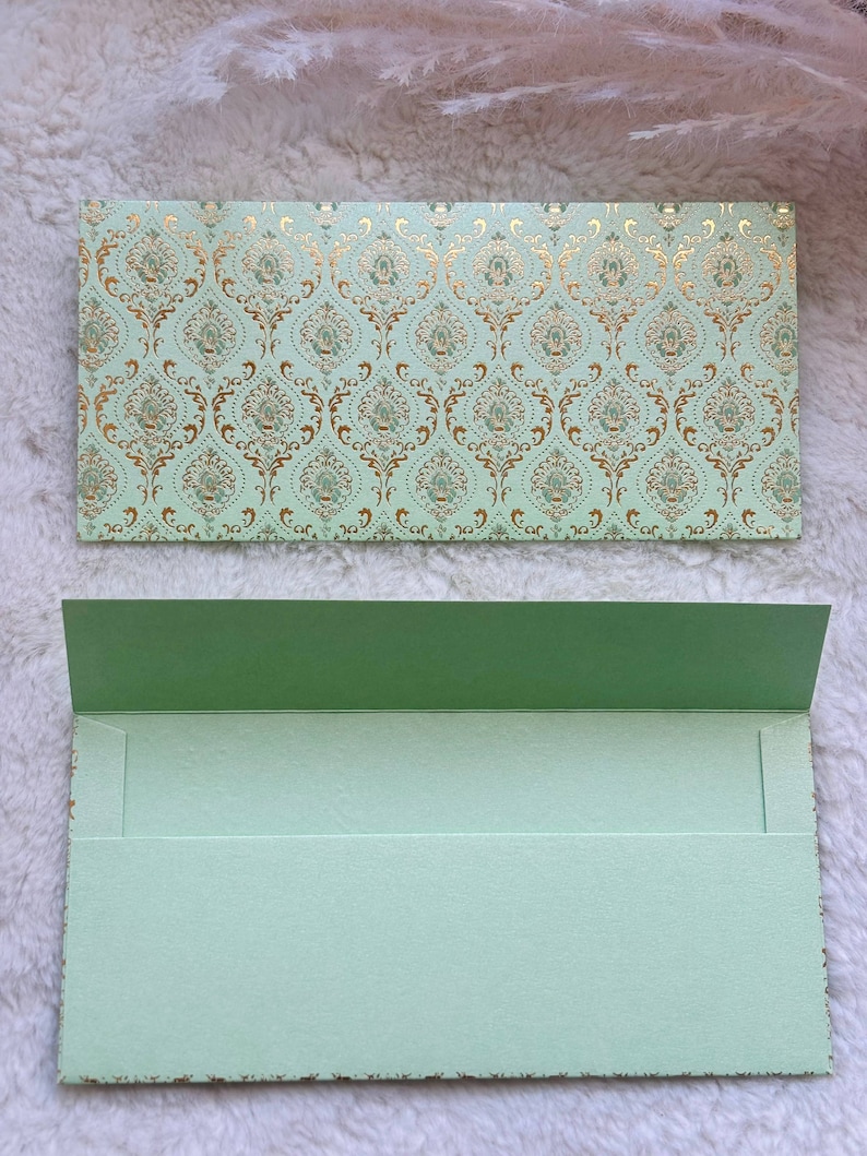 May include: A light green envelope with a gold and green patterned design. The envelope is folded in half and has a flap on the top.