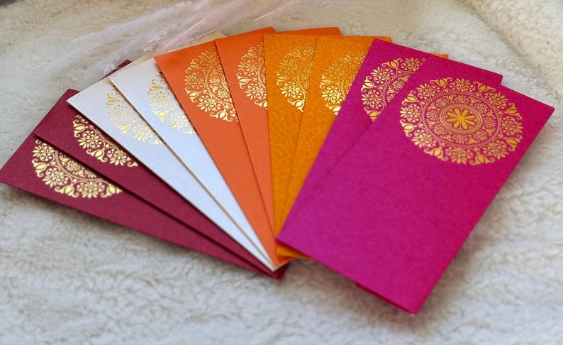 May include: A set of eight decorative envelopes in various colors, including red, orange, yellow, and white. Each envelope features a gold-colored mandala design.
