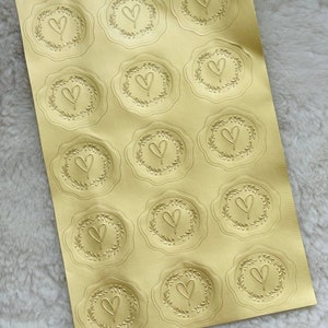 May include: A sheet of gold foil stickers with a heart design in a wreath. There are 16 stickers on the sheet.