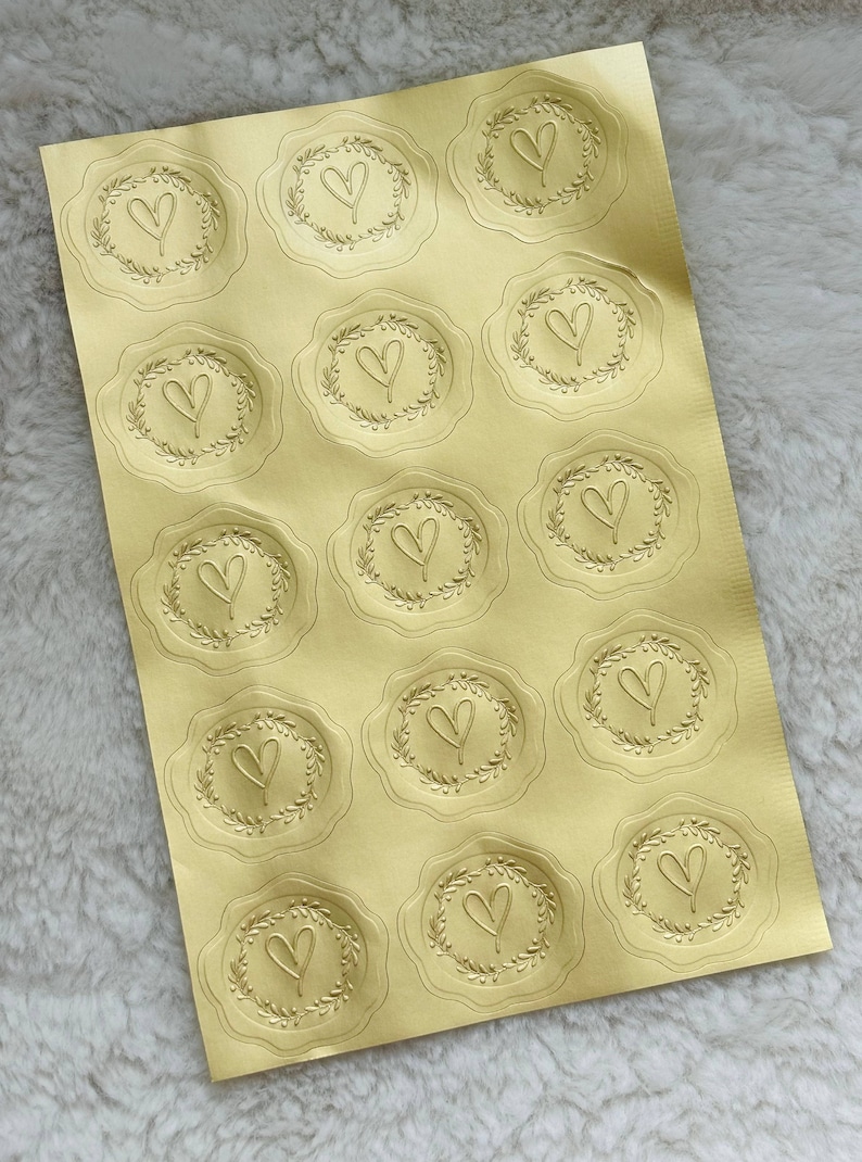 May include: A sheet of gold foil stickers with a heart design in a wreath. There are 16 stickers on the sheet.