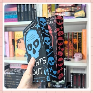 May include: A hand holds three books with decorative covers. The first book has a blue skull design with the title "Nights Out" and the author's name, Navessa Allen. The other two books have repeating patterns of skulls, hearts, and other symbols.