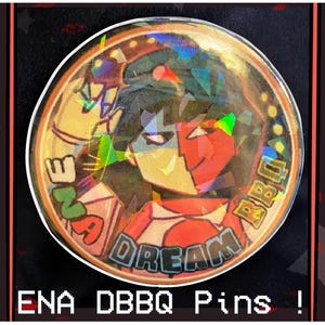 May include: A round button with a holographic finish featuring a cartoon character with red and black hair, wearing a red and white shirt with the text "I'm a Dream BBQ".