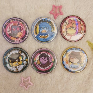 May include: Six round, colourful buttons with cartoon characters and text. The buttons feature characters like a monster, a bird, a dog, and a person. The text on the buttons includes "Martlet", "Dalv", "Clover", "Starlo", and "Leroda".