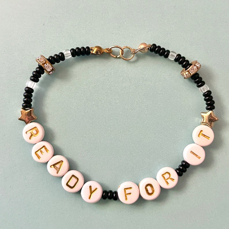 May include: Black and white beaded bracelet with gold letters spelling "READY FOR IT".