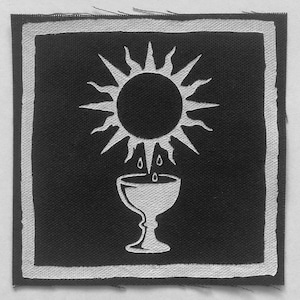 May include: A square fabric patch featuring a black background with a white border. The design displays a white sun with radiating points positioned above a white chalice, with three small white droplets falling from the sun into the cup.