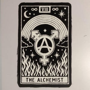 May include: A rectangular black and white embroidered patch featuring a central symbol combining gender and anarchy icons. The design includes a rainbow arch, stars, a crescent moon, and flames at the base, with the text THE ALCHEMIST and VIII.