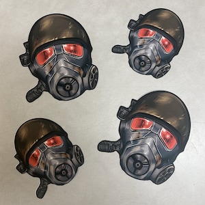 May include: Four gas mask stickers featuring a dark grey and silver colour scheme. The gas masks have red lenses and a dark grey helmet.