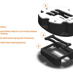 May include: A black and white shifter plate with the text "PLabs" on it. The plate is disassembled into three parts: a base, a spring retainer, and a shifter plate. The parts are labeled A, B, and C.