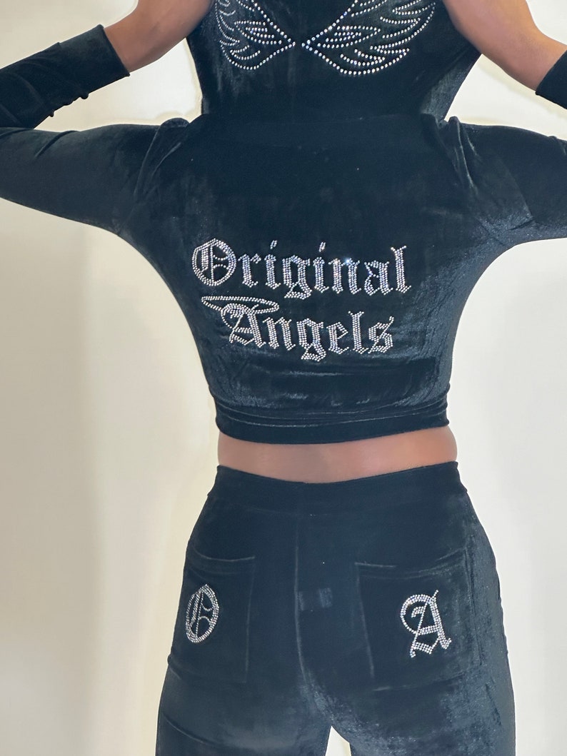 May include: Black velvet tracksuit with a cropped hoodie and matching pants. The hoodie features a rhinestone design of wings and the text "Original Angels". The pants have a rhinestone "O" on the left back pocket and a rhinestone "A" on the right back pocket.