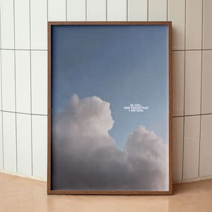 Op de afbeelding: Een ingelijst print met een blauwe lucht en witte wolken. De tekst "Be still and know that I am God." is in wit op de wolken gedrukt.