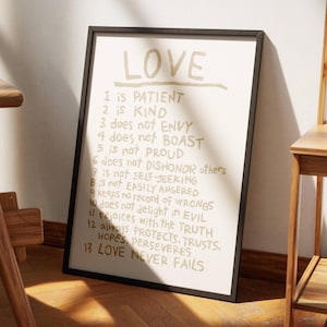 May include: A black framed print with a white background and gold text. The text reads "LOVE" and lists 13 qualities of love, including patient, kind, does not envy, does not boast, is not proud, does not dishonour others, is not self-seeking, is not easily angered, keeps no record of wrongs, does not delight in evil, rejoices with the truth, always protects, trusts, hopes, perseveres, love never fails.