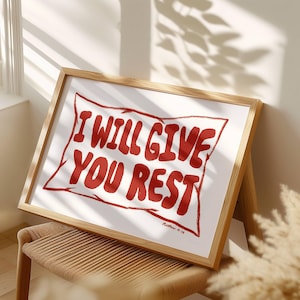 Pode incluir: Uma impressão emoldurada com fundo branco e texto vermelho que diz "I WILL GIVE YOU REST" com a referência bíblica "Mateus 11:28" abaixo do texto.