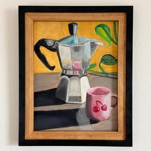 May include: A framed painting featuring a silver moka pot with a black handle and a pink mug decorated with two red cherries. The background is a vibrant yellow with green leaves, and the objects cast long dark shadows on a flat surface.