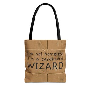 May include: A tote bag with a cardboard design and black handles. The bag features the text "I'm not homeless I'm a cardboard WIZARD" in black letters. The bag is made of a durable material.