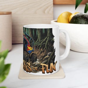 May include: White ceramic mug featuring a colorful off-road vehicle racing through a forest. The vehicle is red, blue, and yellow. The mug has the text "KS FOR FUN" in gold lettering.