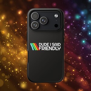 May include: Black phone case with a multi-lens camera array. The case features the text "DUDE I SAID FRIENDLY" in white, with a colorful striped design. The background has a bokeh effect with orange, yellow, and blue lights.